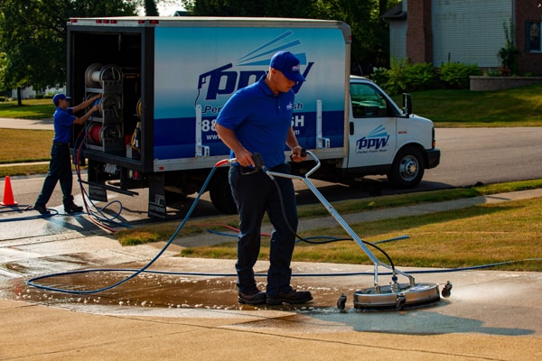 Power washing technician using surface cleaner to wash a driveway while another technician works in the background