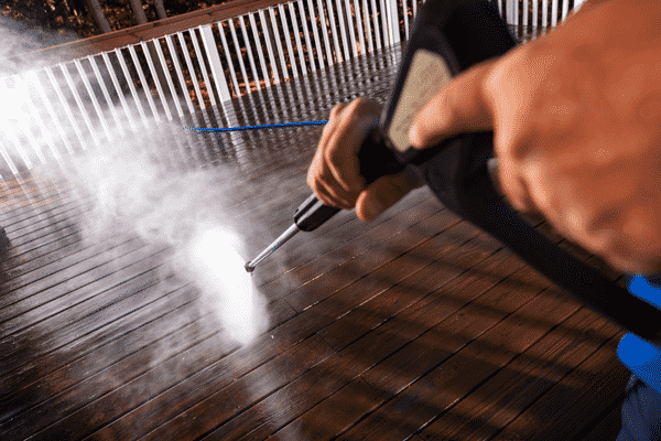 Two hands holding power washing wand and washing a wooden deck