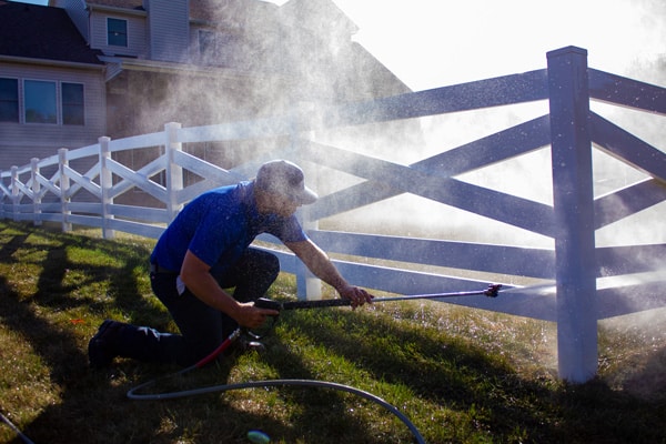 Power washing technician kneeling down to safely wash a white vinyl fence