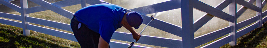 Power washing technician bending over to safely wash a white vinyl fence