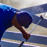 Power washing technician bending over to safely wash a white vinyl fence