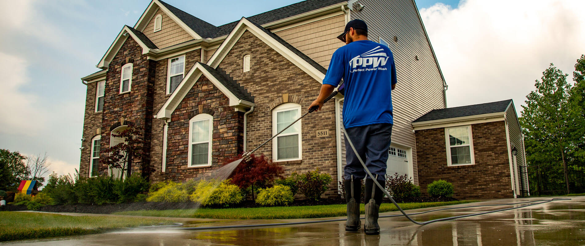Perfect Power Wash technician spraying siloxane sealer on concrete driveway in front of brick and vinyl home