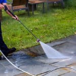 Power washing technician using safe pressure to wash stone back patio with furniture moved to the side