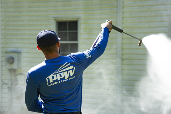 Perfect Power Wash technician using safe pressure to remove contaminants from white vinyl siding