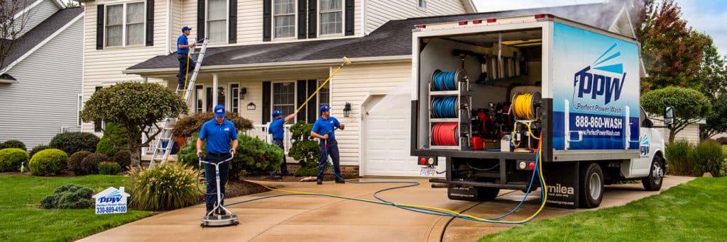 4 power washing technicians treating a roof, washing concrete, scrubbing gutters, and washing a house next to company truck