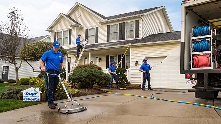 4 power washing technicians treating a roof, washing concrete, scrubbing gutters, and washing a house next to company truck