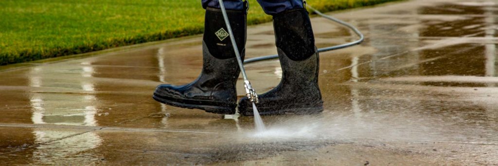Power washing technician using safe pressure on a concrete driveway using a wand