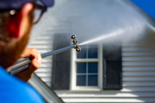 Technician Power Washing a White Sided House