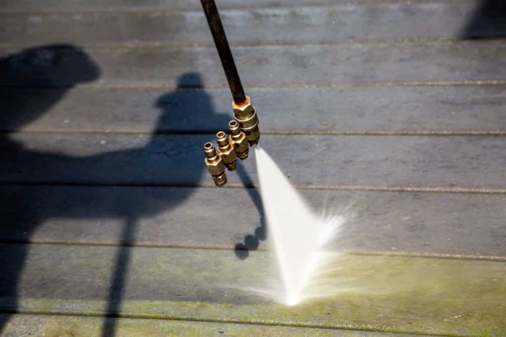 point-of-view of power washing wand cleaning green algae off a dark wooden deck