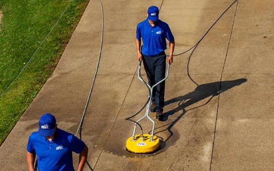 Aerial view of two power washing technicians using circular surface cleaners to wash a concrete driveway